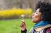 Black woman blowing dandelion seeds in park