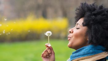 Black woman blowing dandelion seeds in park