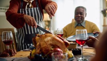 Close up of black woman carving roast turkey during Thanksgiving dinner at dining table.