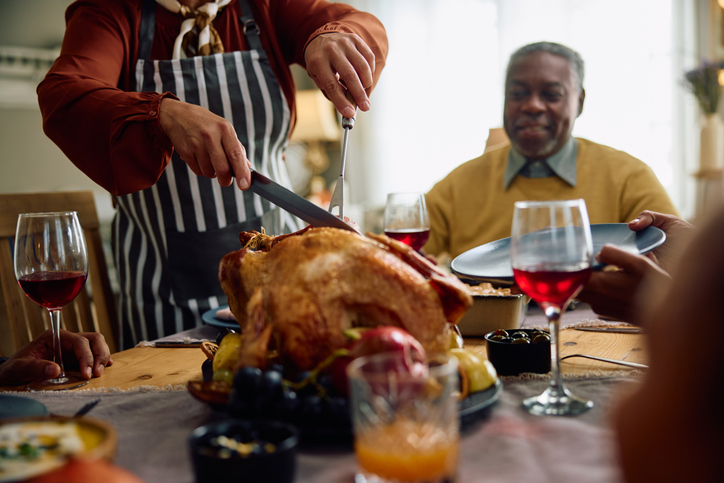 Close up of black woman carving roast turkey during Thanksgiving dinner at dining table.