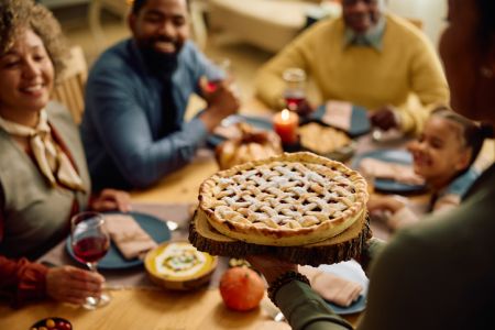 Close up of black woman serving Thanksgiving pie during family meal.