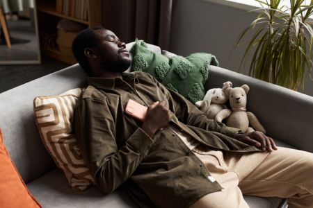 Black man falling asleep on couch at home with smartphone on chest