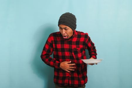 Young Asian man is feeling nauseous while holding white plate, isolated on a blue background