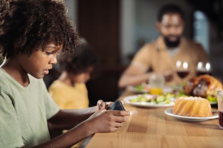 African American boy watching something on mobile phone at dining table