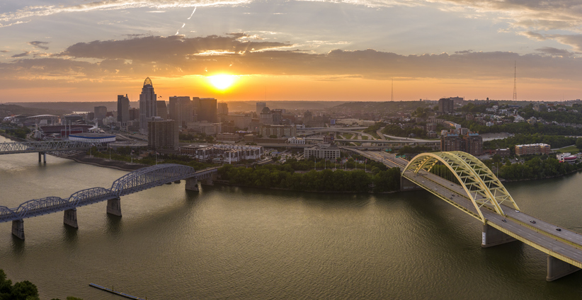 Highway traffic with driving cars on bridge in downtown district of Cincinnati city in Ohio, USA. American city skyline with brightly illuminated high commercial buildings at sunset
