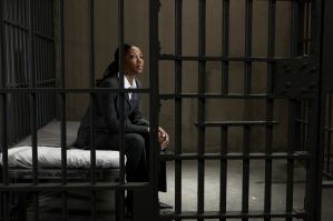 Young businesswoman sitting on bed in prison cell, looking away