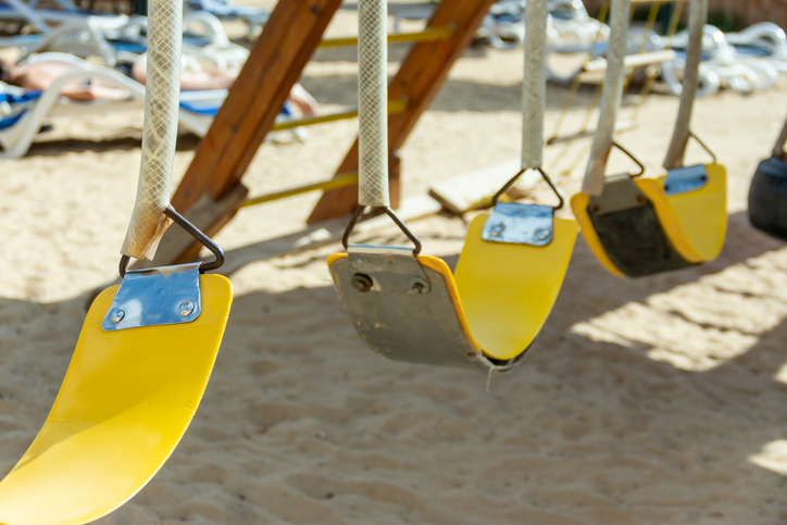 Empty yellow swings on sandy beach playground illuminated by sunshine