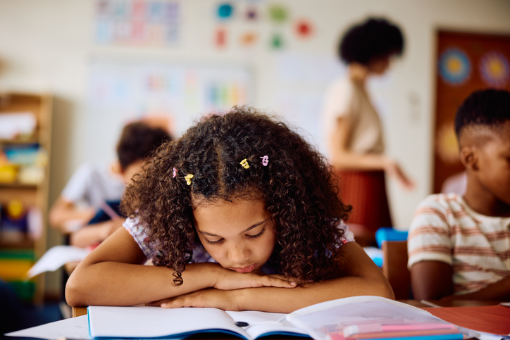Schoolgirl leaning on desk in class, daydreaming
