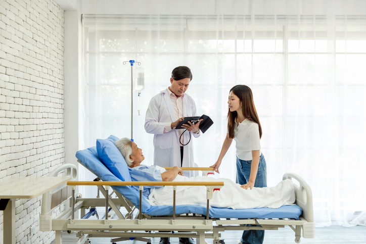 A general practitioner examines a senior woman in a hospital bed while her daughter listens attentively. The scene highlights healthcare, elderly care, and medical consultation in a modern clinic.