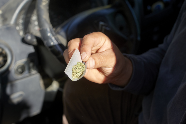 Driver rolling marijuana joint inside vehicle, demonstrating dangerous impairment and potential traffic safety risks during driving
