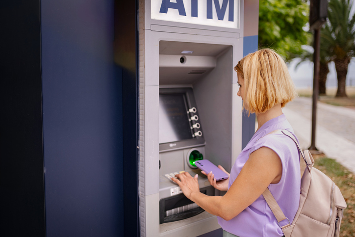 Young woman withdrawing cash at ATM using smartphone