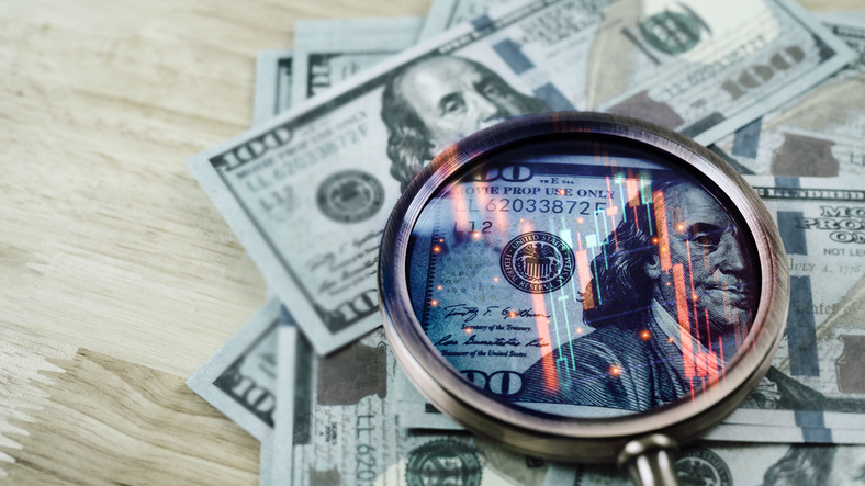 Closeup on magnifier glass with Benjamin Franklin on US dollar banknote and stock market graph for currency exchange and Interest rates concept.