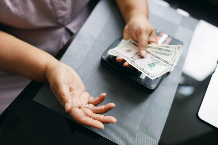 Upper angle view of african american female hands with puzzled gesture holding and counting us dollars from purse and its small sum of money to pay for high prices of utilities and rent