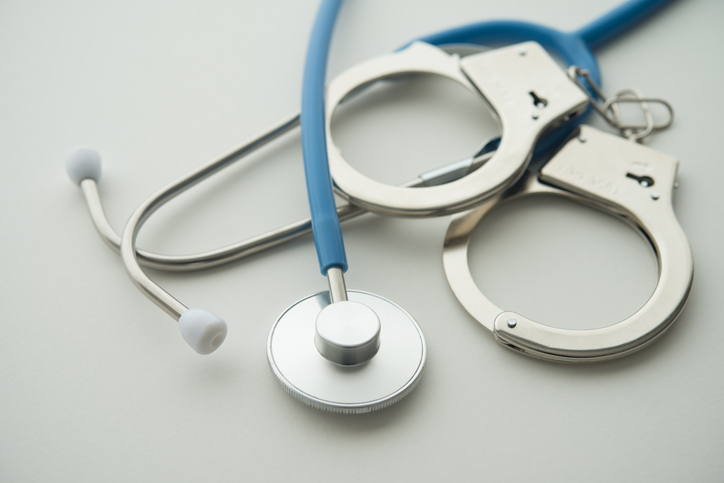 Handcuffs and stethoscope on white background.