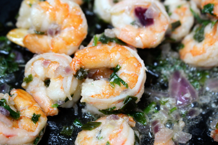 Cooking shrimps with spices and chopped red onions in a frying pan