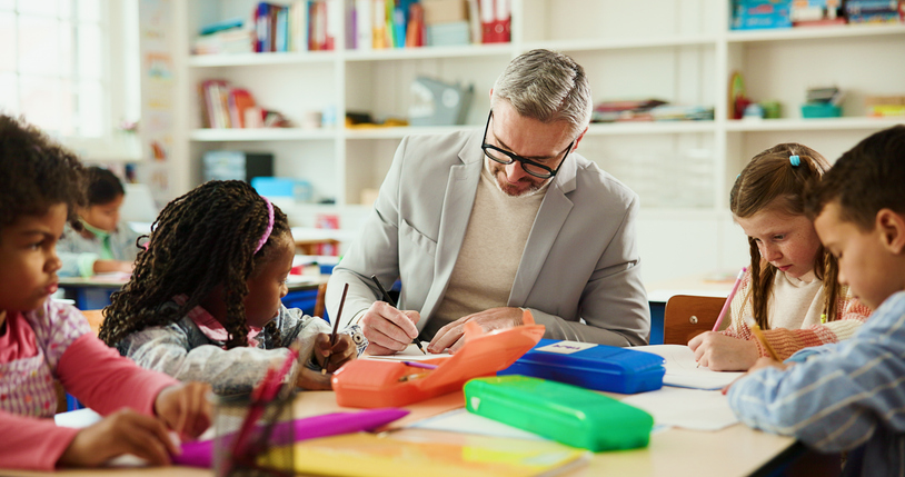 Education, learning or writing with students and teacher at desk in classroom for child development. Future, growth or notes with educator man teaching kids in elementary school class for lesson