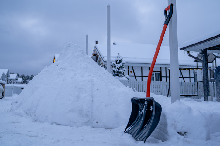 Snow shovel standing high snow pile near suburban home driveway. Manual snow removal after snowfall