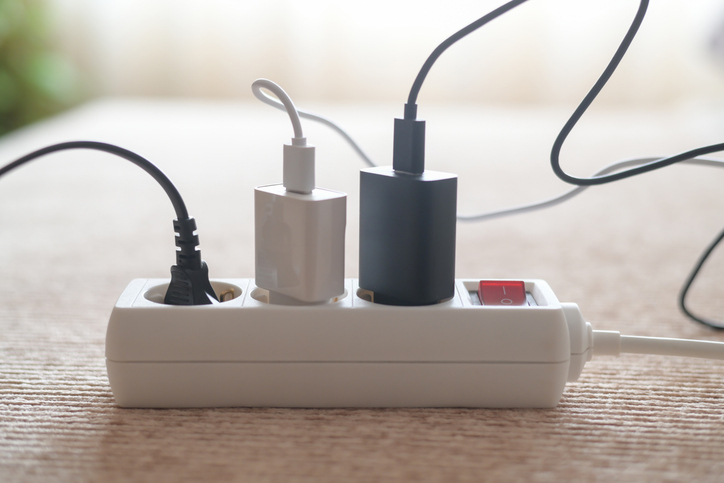 Electric power strip loaded with multiple chargers and cables plugged in, showing active electricity use and potential energy consumption, overload risk, and standby power draw