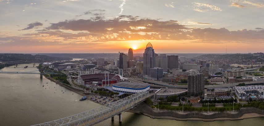 Cincinnati city, Ohio, USA with bridge highway traffic driving cars in downtown district. American city skyline with brightly illuminated high commercial buildings at sunset