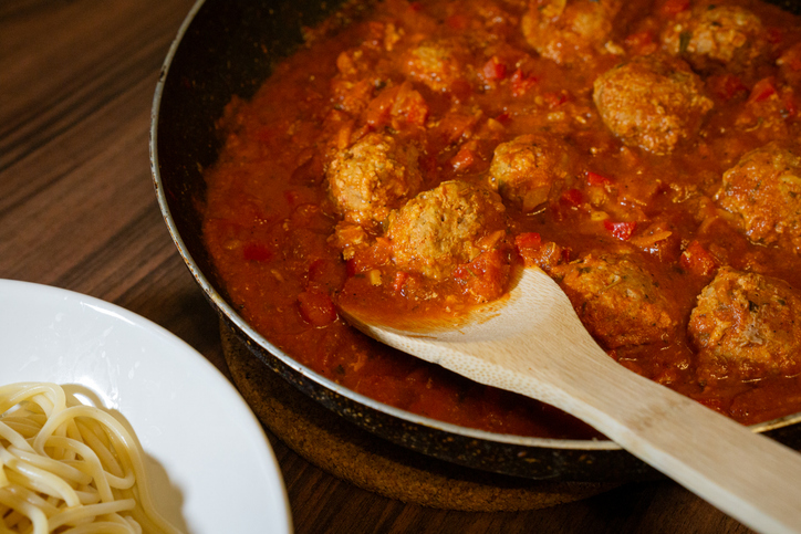 Meatballs simmering in tomato sauce in a pan.