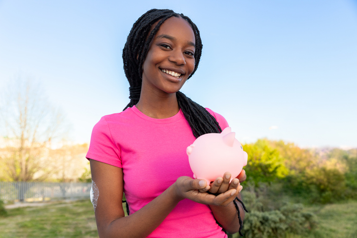 Black girl smiling holding piggy bank outdoors saving money