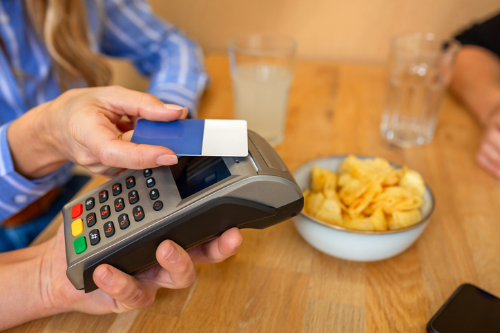 Unrecognizable woman paying contactless with credit card at restaurant terminal