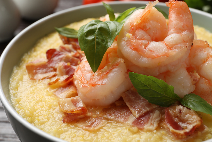 Fresh tasty shrimps, bacon, grits and basil in bowl on table, closeup