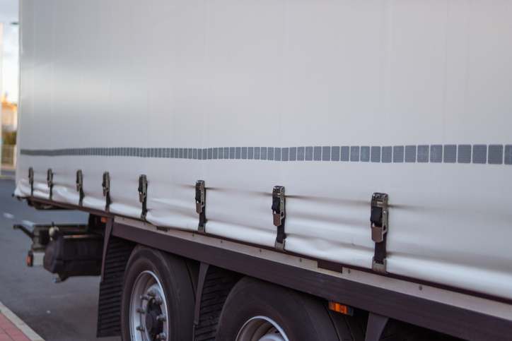 White cargo truck side view showcasing the tarpaulin cover with metal latches and reflective strips, representing freight transport, logistics, and delivery during the day