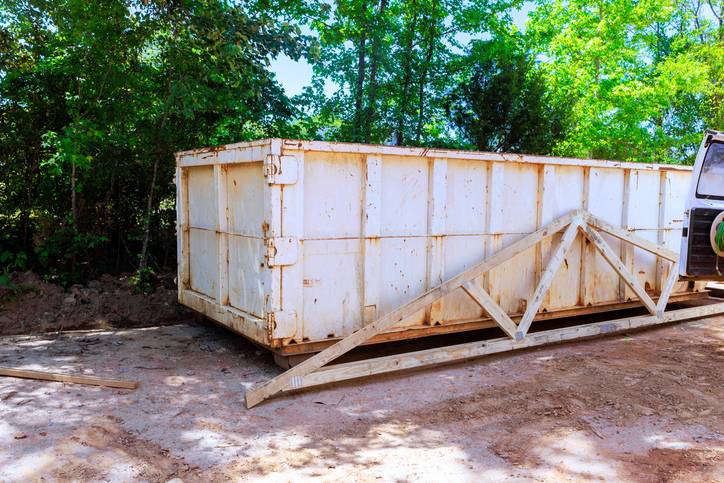 Large white dumpster placed in wooded area for waste collection