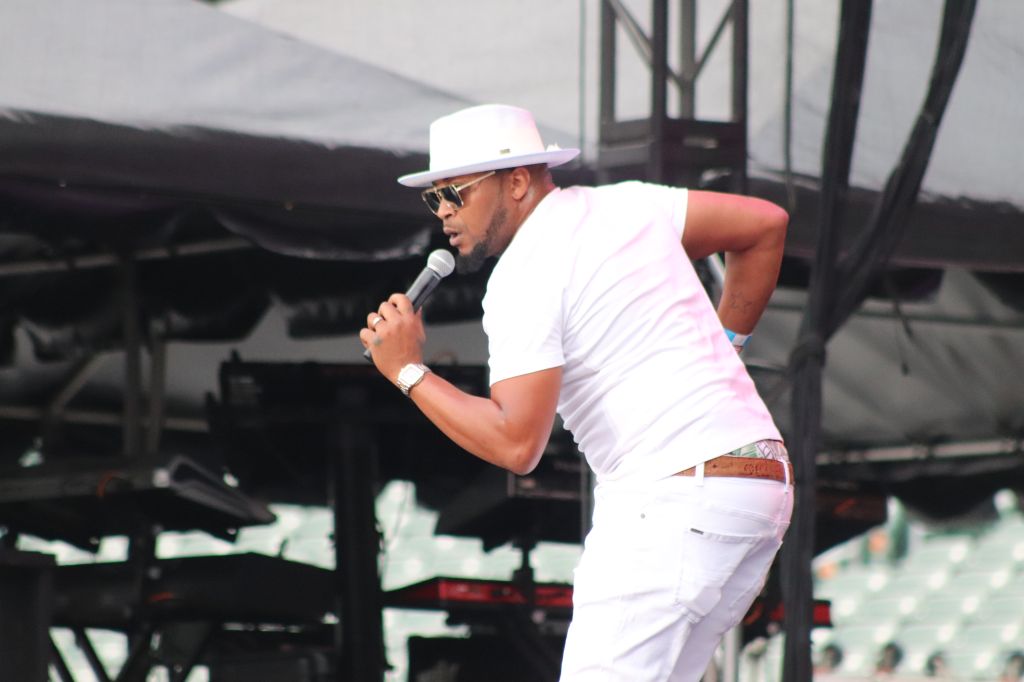 A man in a white hat and shirt performing on stage with a microphone.