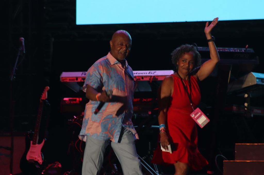 Two people on stage, a man in a colorful shirt and a woman in a red dress, dancing and performing.