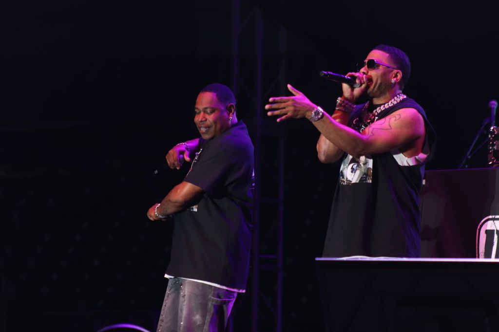 Two men performing on stage, one singing into a microphone and the other standing beside him.