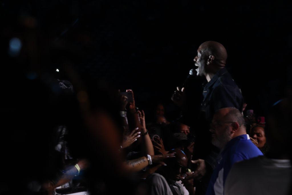 A person on stage performing before a crowd in a dark setting.