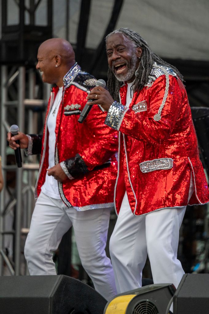 Two men in red sequined jackets performing on stage, one singing into a microphone and the other playing an instrument.