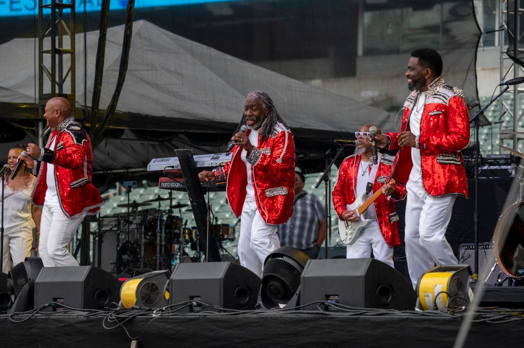 A group of musicians in red sequined outfits performing on stage, with various musical instruments and equipment visible.