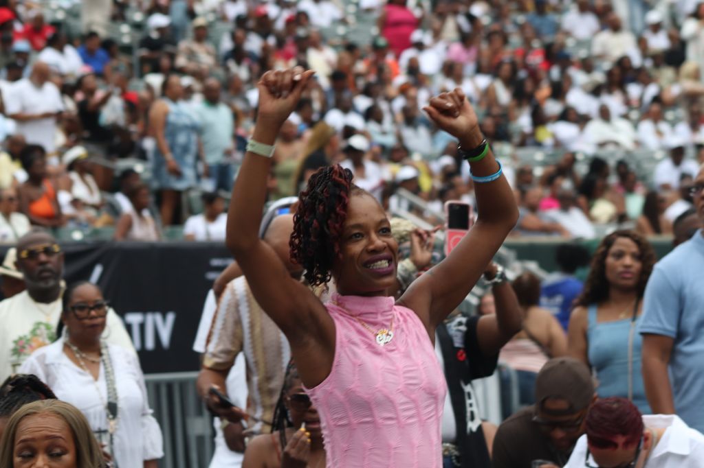 A crowd of people at an event, with a woman in a pink shirt raising her arms in celebration.