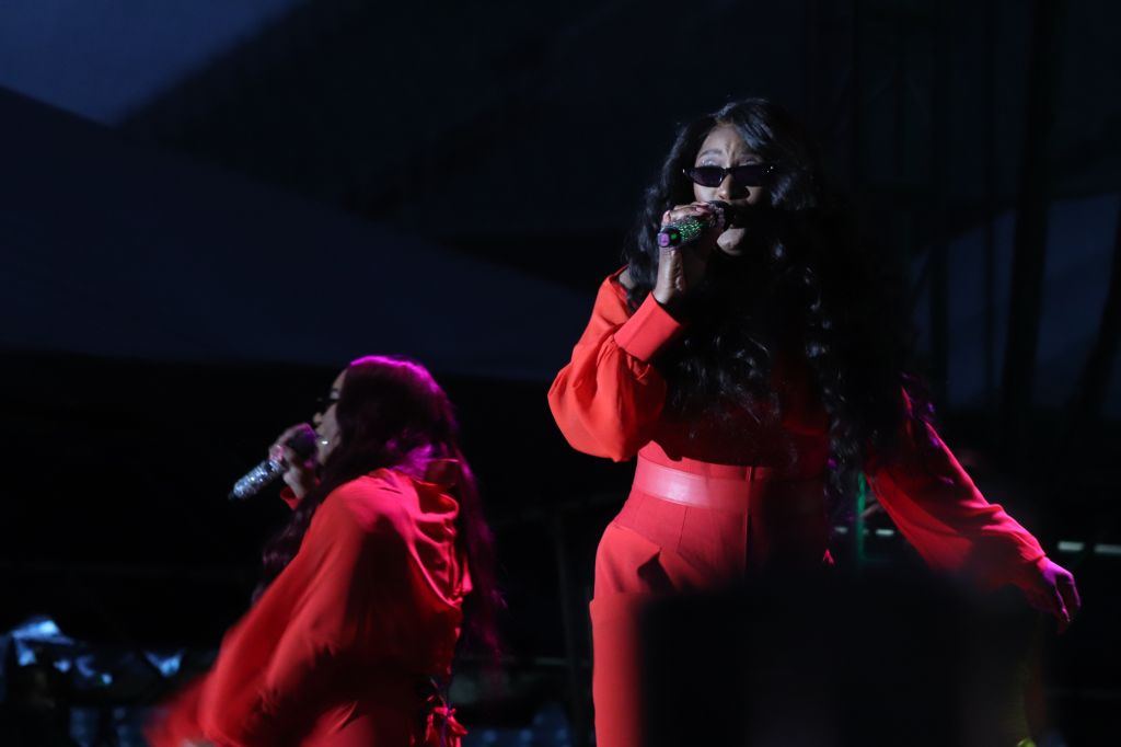 Two performers on stage in red outfits singing into microphones in a dark setting.