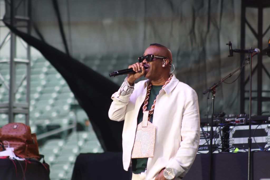 A man wearing sunglasses and a white jacket performing on stage, holding a microphone and singing.