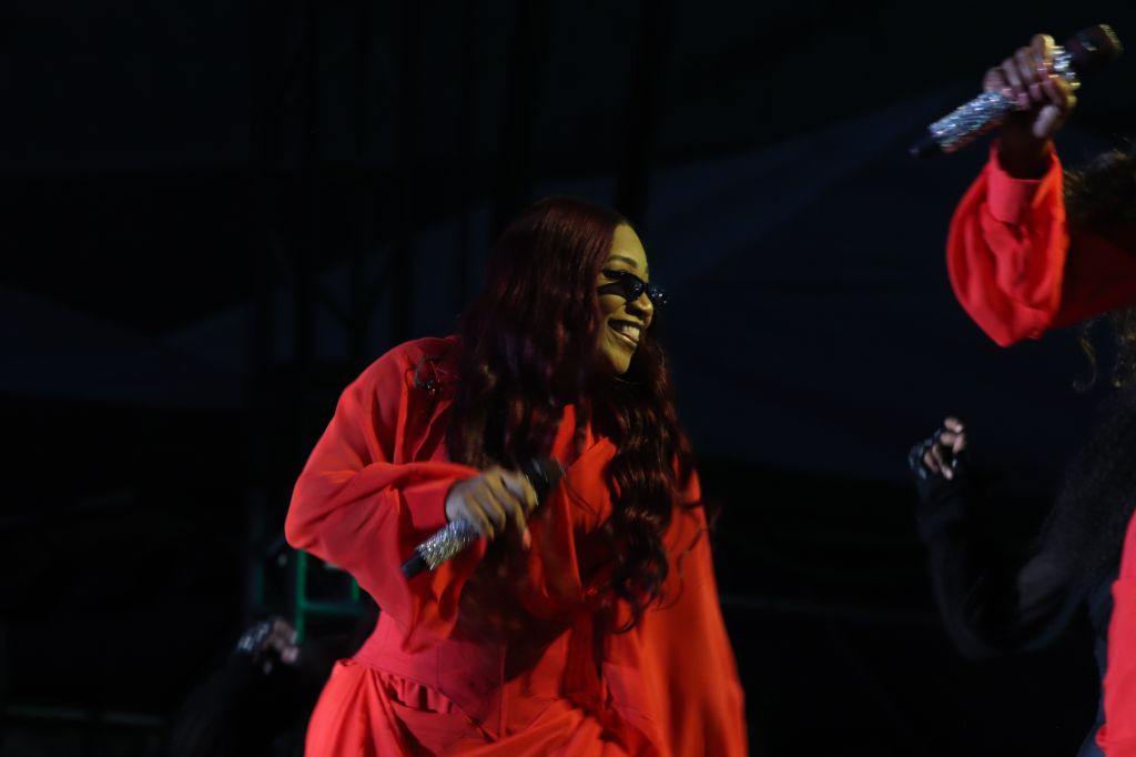 A woman in a bright red outfit performing on stage, with her long dark hair flowing as she sings into a microphone.