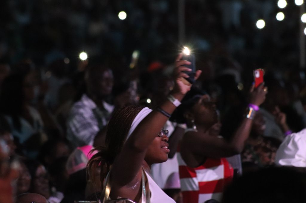 Crowd of people holding up phones and cameras in a dark setting, with lights and reflections visible.