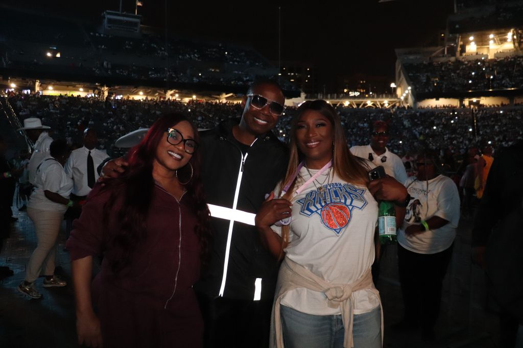 Three people posing for a photo at a crowded outdoor event, with the New York Knicks logo visible on one person's shirt.
