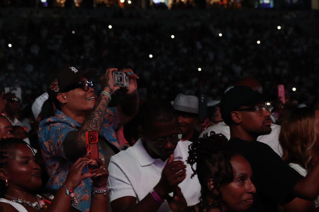 A large crowd of people in a dark setting, many holding up their phones to capture the moment.
