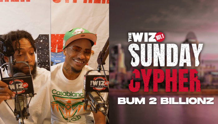 Two men smiling and speaking into microphones in a studio setting, with "The Wiz 101.1 Sunday Cypher" text visible.